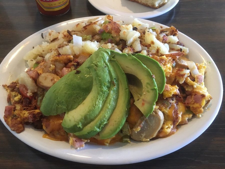 A plate of chopped potatoes, ham and eggs topped with a fan of sliced avocado.