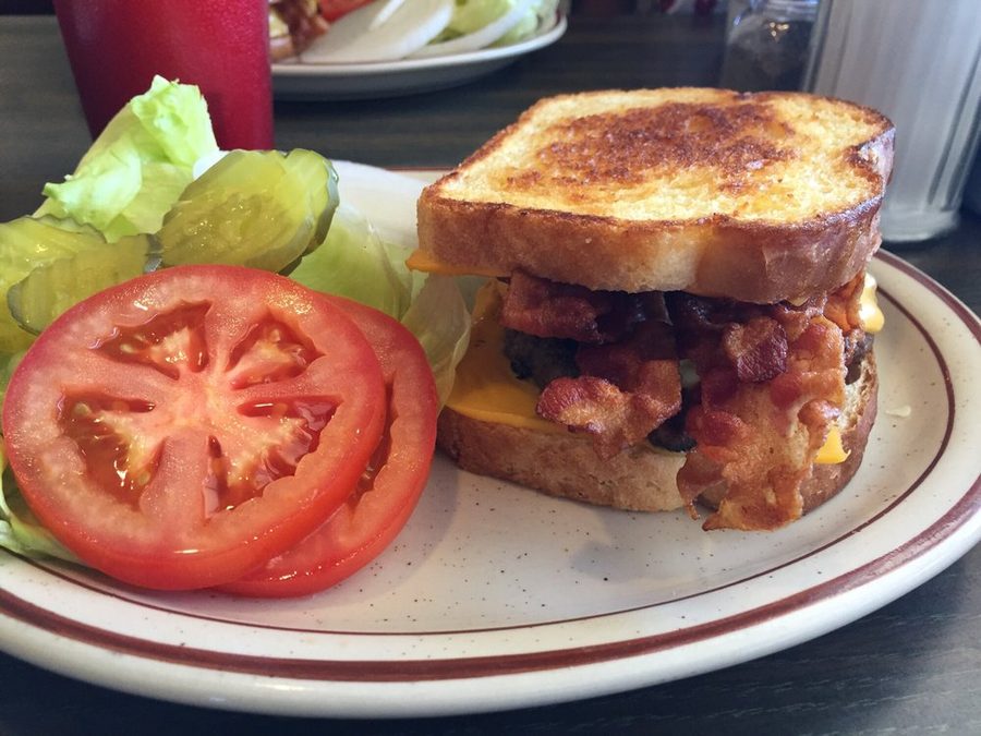 A grilled bacon and cheese sandwich on toasted bread, served with thick tomato slices, lettuce and pickles.