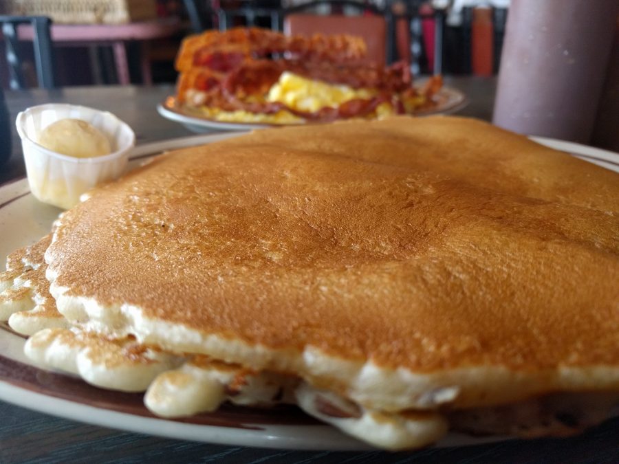 A hotcake wider than the plate it is served on, with a cup of whipped butter beside it.